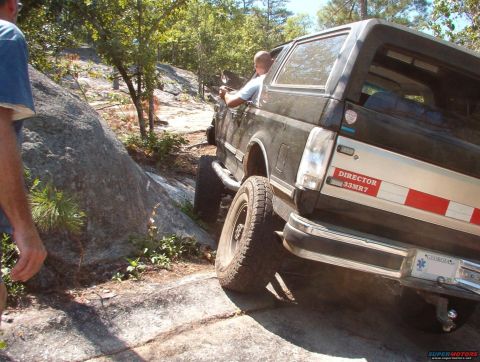 1988 Ford Bronco - A black Ford Bronco navigates a rocky off-road trail, its rear end angled towards the camera.