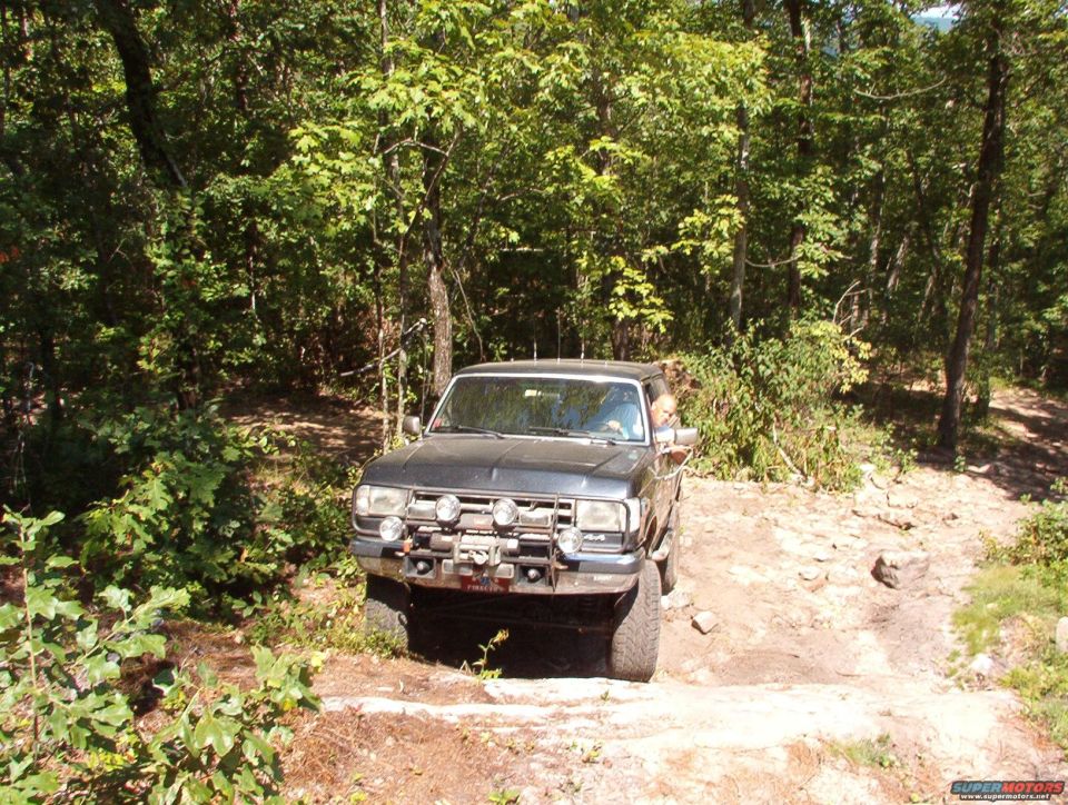 Dark gray 1988 Ford Bronco with off-road lights and winch on a dirt trail