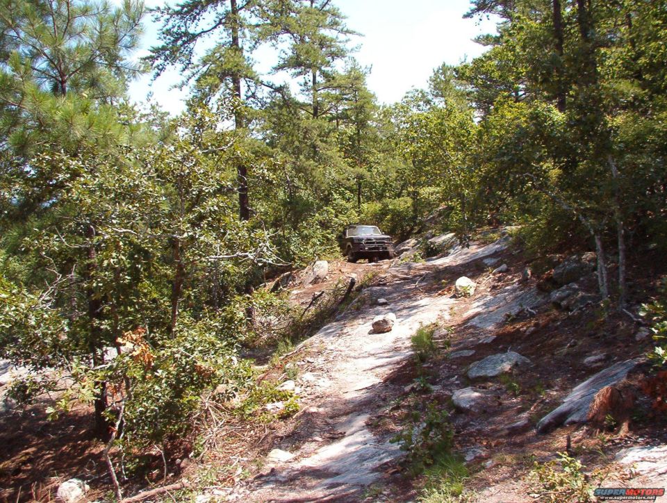 1988 Ford Bronco driving up a steep, rocky, wooded trail
