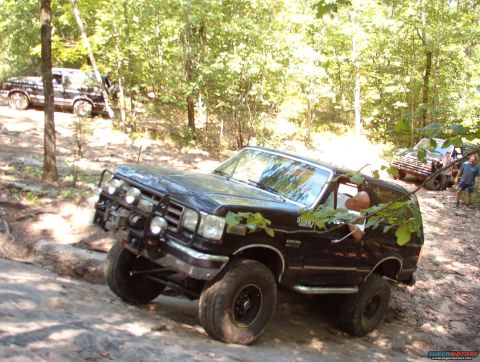 1988 Ford Bronco - A black Ford Bronco navigates a challenging off-road course with another vehicle in the background.