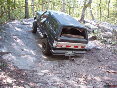 1988 Ford Bronco - This dark SUV is shown navigating a challenging rocky trail, demonstrating its off-road capabilities.