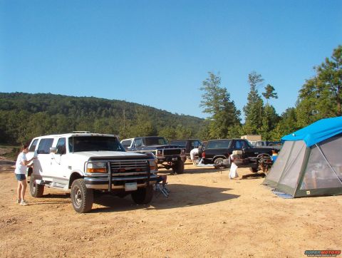 1988 Ford Bronco - Several trucks, including a white Ford Bronco, are parked at a campsite on a sunny day.