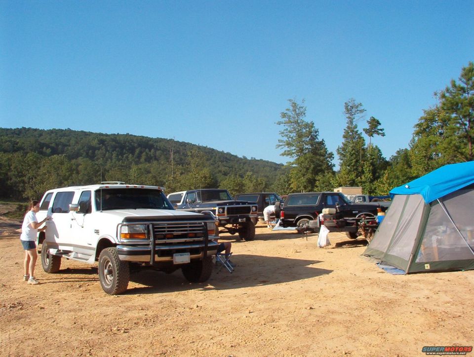 White Ford Bronco and several other trucks parked at a campsite with a tent