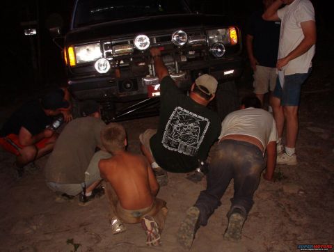 1988 Ford Bronco - A group of people are working on the front of a vehicle at night, with auxiliary lights illuminating the scene.