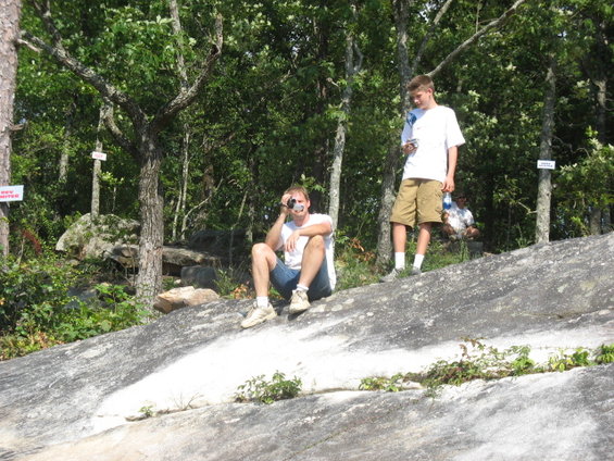 Two men in a wooded area, one taking a photo