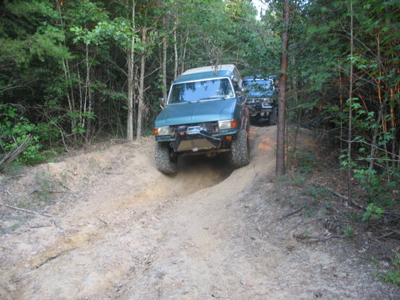 Two off-road SUVs on a sandy trail in the woods.