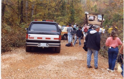 1988 Ford Bronco - The rear of a black 1988 Ford Bronco with red and white reflective striping on the tailgate is parked on a dirt road. Several people and ot…