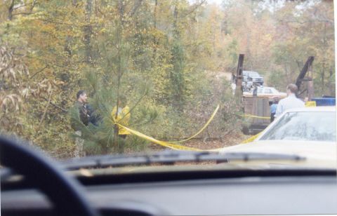 1988 Ford Bronco - A yellow crime scene tape is strung across a wooded area with a man in a dark jacket standing near a pine tree. In the background, several…