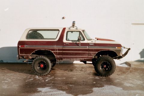 1979 Ford Bronco - A modified 1978 Ford Bronco with a two-tone paint job and off-road tires sits parked outside a building.