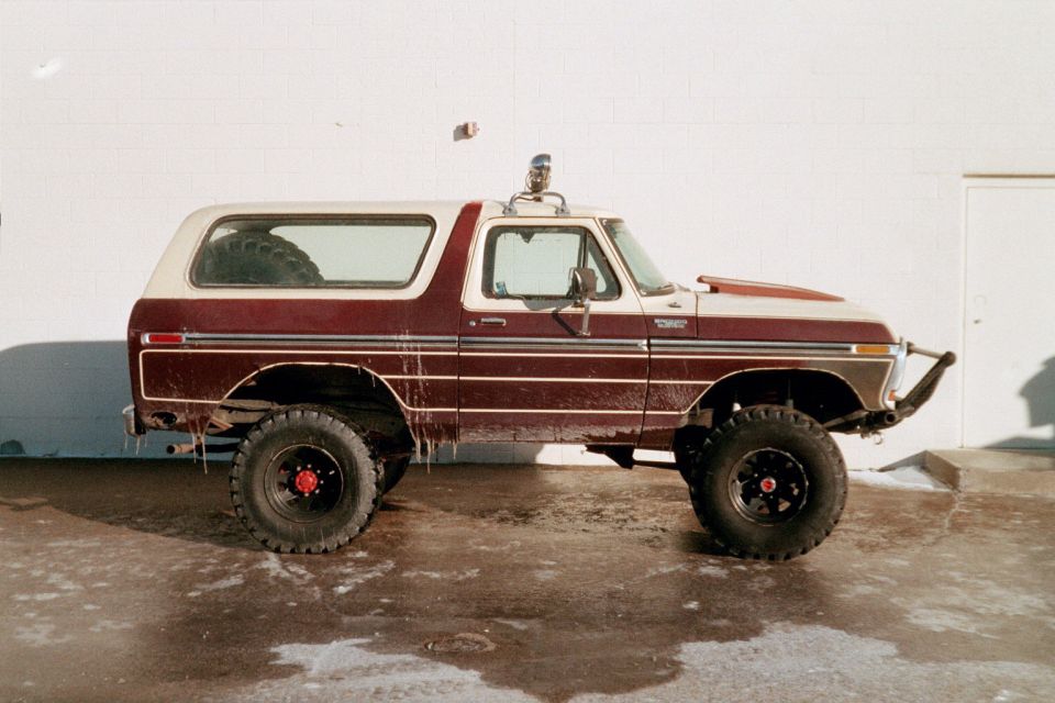 Maroon and white Ford Bronco with aftermarket bumper and hood scoop, seen from the side