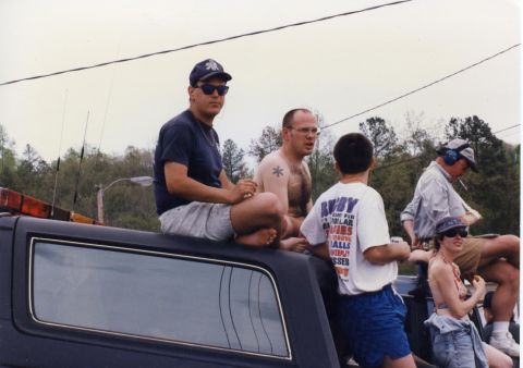 1988 Ford Bronco - Several people are sitting on top of a dark-colored vehicle, possibly a hearse or a large SUV, with emergency lights visible on the front.…