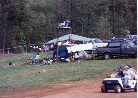 1988 Ford Bronco - A dark gray Ford pickup truck is parked on a grassy area next to a tent and a viewing stand. Several people are relaxing in chairs and on t…