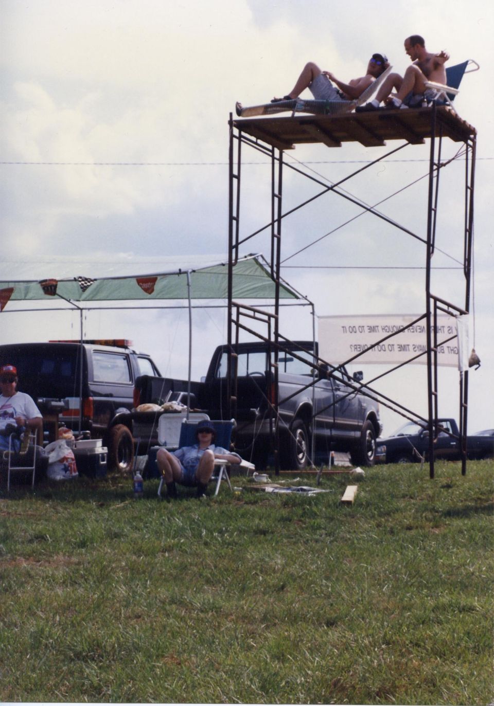 Two men on a scaffolding platform above a black Ford Bronco and pickup truck.