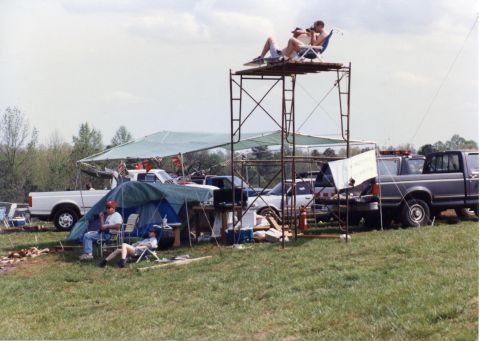 1988 Ford Bronco - A group of people are gathered at an outdoor event with tents and several pickup trucks visible. Two people are seated on a raised platform…