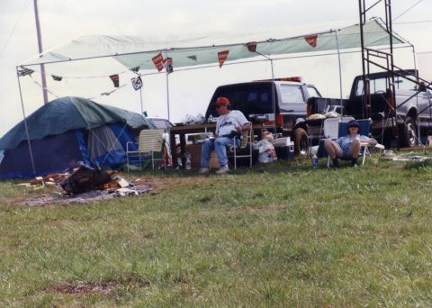 1988 Ford Bronco - A 1988 Ford Bronco is parked under a canopy next to a tent and other vehicles. Two people are relaxing in chairs in front of the vehicles.