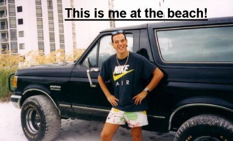 1988 Ford Bronco - A man in a black Nike t-shirt and patterned shorts stands with his hands on his hips in front of a black Ford Bronco on a sandy beach. A ta…