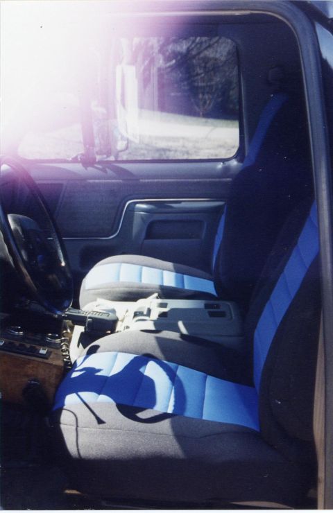 1988 Ford Bronco - The interior of a Ford Bronco shows the driver's side seat and dashboard. The seats are upholstered in dark fabric with blue accents.