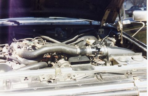 1988 Ford Bronco - The engine bay of a 1988 Ford Bronco is shown with the hood open. The image focuses on the engine, hoses, and air intake system.