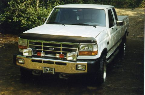 1988 Ford Bronco - A white Ford pickup truck is parked in shallow water with trees in the background. The truck has a chrome bumper with a winch and auxiliary…