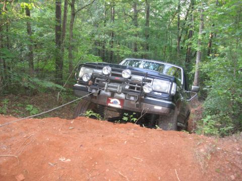 1988 Ford Bronco - A black Ford Bronco is being pulled out of a ditch by a tow rope in a wooded area. The vehicle is angled upwards, with its front end elevat…