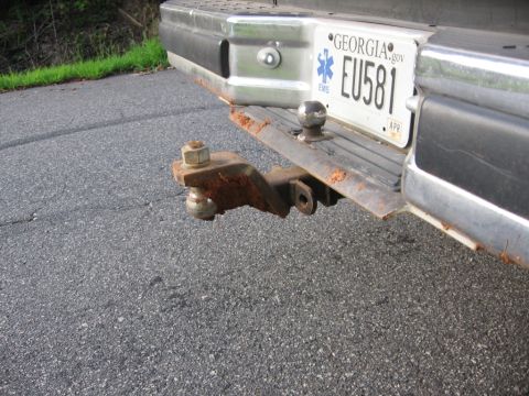 1988 Ford Bronco - The rear bumper of a vehicle shows a rusty trailer hitch with a ball mount. A Georgia license plate with the text "EU581" is visible above…