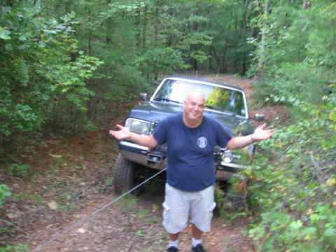 1988 Ford Bronco - A man stands in front of a dark colored SUV, possibly a Ford Bronco, with his arms outstretched. The vehicle is on a dirt path surrounded b…