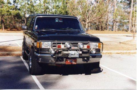1988 Ford Bronco - Front view of a black Ford Bronco with a brush guard, winch, and multiple auxiliary lights mounted on the front.