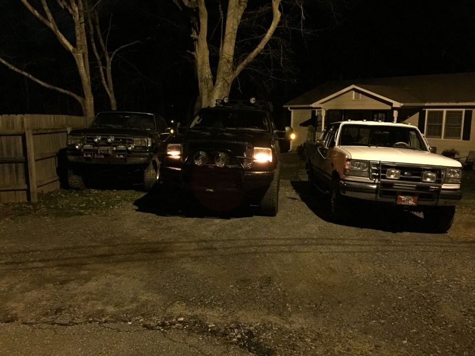 Three pickup trucks parked at night in a driveway.
