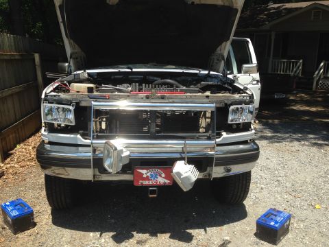1997 Ford F-250 - Front view of a white Ford pickup truck with the hood open, parked outdoors on a gravel surface. Two blue batteries are placed on the groun…