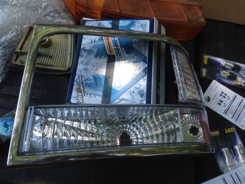 1997 Ford F-250 - A chrome-trimmed headlight assembly is shown with packaging for LED bulbs in the background. The headlight has a clear lens with a textured…