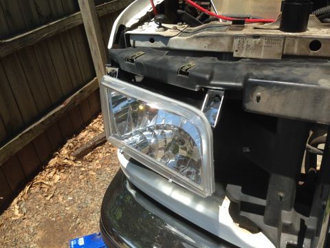 1997 Ford F-250 - A close-up view of a new headlight assembly being installed on the front of a white Ford F-250 pickup truck. The truck is parked outdoors n…