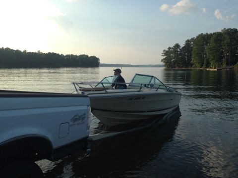 1997 Ford F-250 - A white pickup truck is partially visible on the left, backing a boat into a lake. A person is seated in the boat, which is on a trailer.