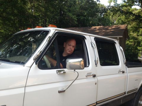 1997 Ford F-250 - A man is sitting in the driver's seat of a white four-door pickup truck. The truck has chrome accents on the door handles and side mirrors,…