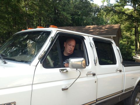 1997 Ford F-250 - A man is sitting in the driver's seat of a white Ford F-250 pickup truck. The truck has amber clearance lights on the roof and is parked ou…