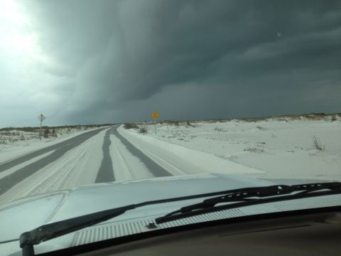 1997 Ford F-250 - The view from inside a vehicle driving on a road covered in sand or snow. Dark, stormy clouds are visible in the sky ahead.