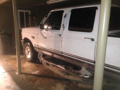 1997 Ford F-250 - A white four-door pickup truck is parked under a covered area with ice and snow accumulated on its lower body and running boards. The scene…
