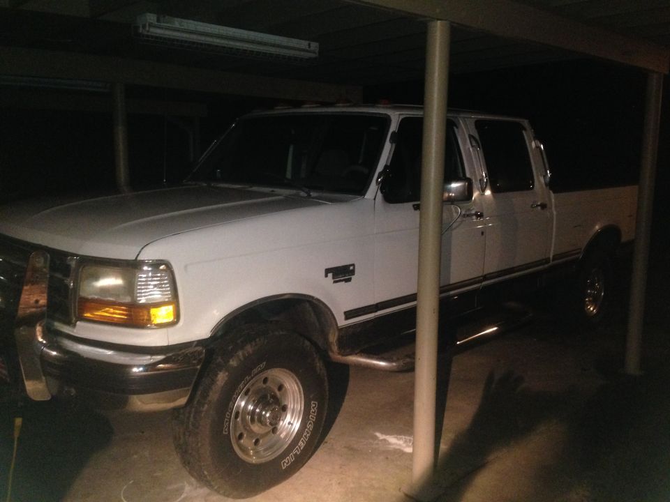 White four-door pickup truck parked under a cover at night, front passenger side view.