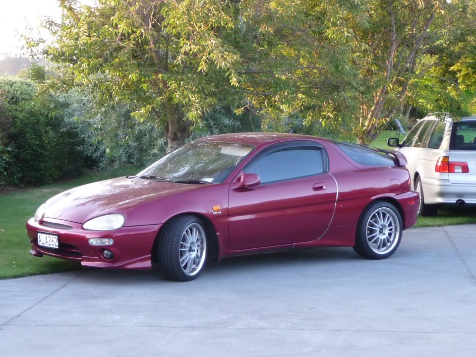 Maroon 1993 Mazda MX-3 coupe parked on a driveway with trees in the background.
