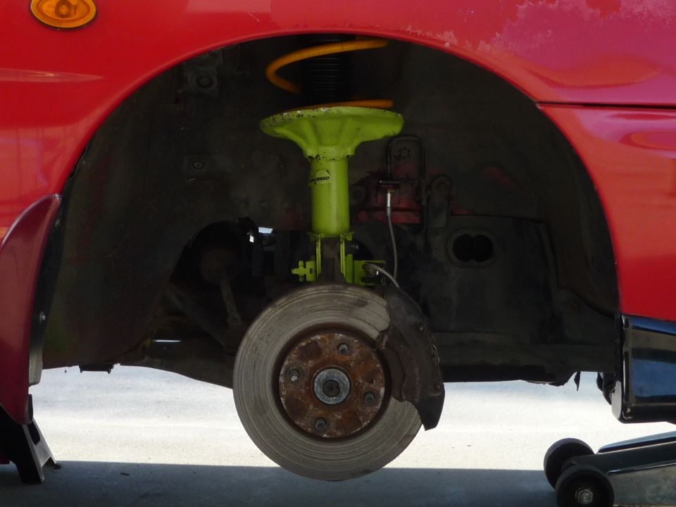 Red vehicle's front suspension and brake assembly with green coilover and yellow spring.