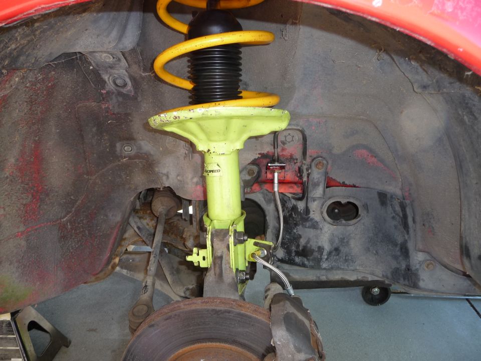 Front suspension of a red Mazda MX-3 with yellow coilover and green strut.