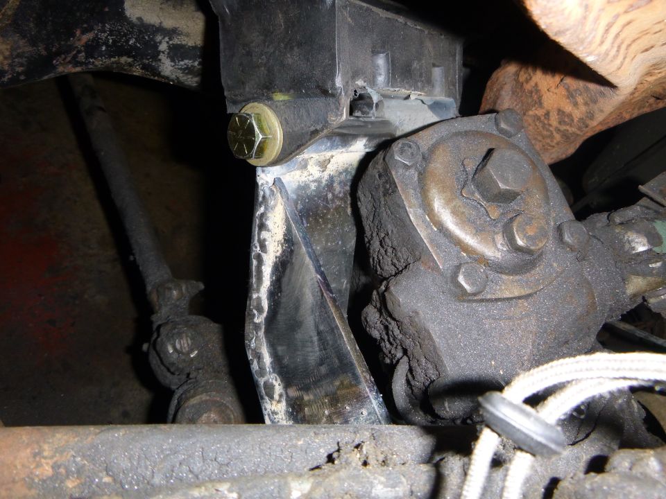 Close-up of a greasy steering gear box and bracket on a vehicle undercarriage.