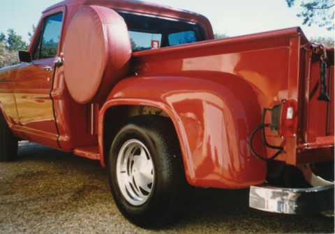 1967 Ford F-100 - A red 1967 Ford F-100 pickup truck is viewed from the rear quarter, showing its spare tire mounted externally.