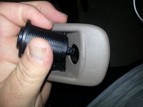 1994 Ford Bronco - Photo of a beige interior bezel with a black 12V socket barrel being removed by hand.