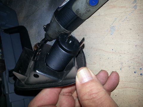1994 Ford Bronco - Photo of a rotary tool modifying a black 12V power-socket barrel mounted in a bracket.