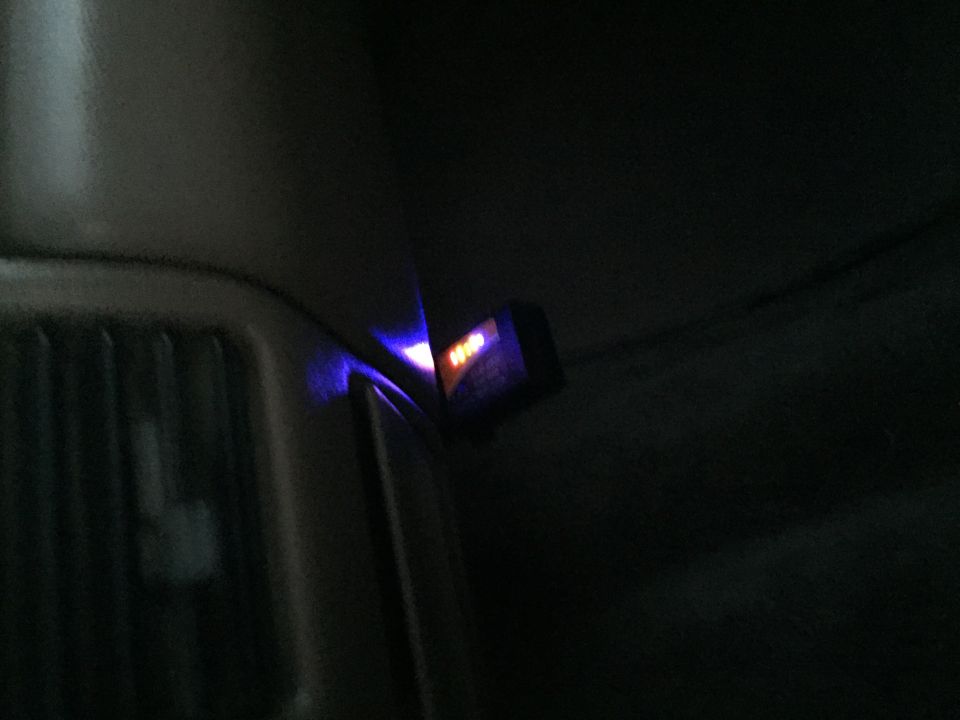 Close-up of a small electronic device with orange and purple lights inside a vehicle.