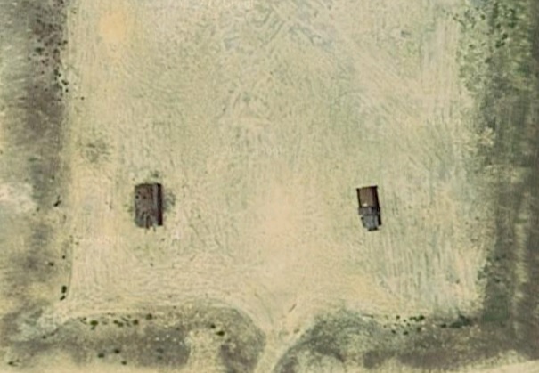 Two trucks parked in a dirt field, viewed from above.