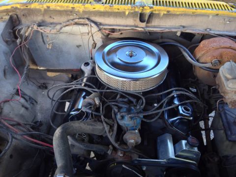 1979 Ford Bronco - The engine bay of a vintage yellow Ford Bronco shows a V8 engine with a chrome air cleaner and various hoses and wiring. The engine appears…