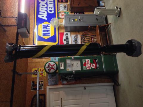 1979 Ford Bronco - A black and yellow striped drive shaft is mounted above a vintage green Sky Chief gasoline pump. The background shows a garage wall with va…