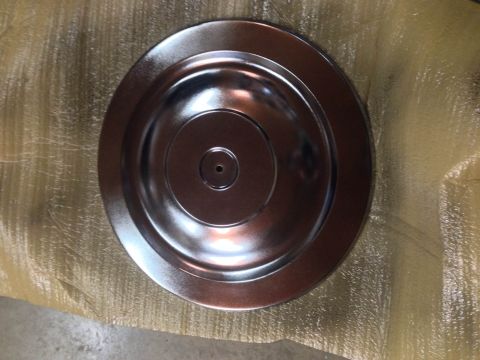 1979 Ford Bronco - A shiny, chrome-like metal hubcap with concentric rings and a central hole is shown from a top-down perspective. It rests on a textured, li…