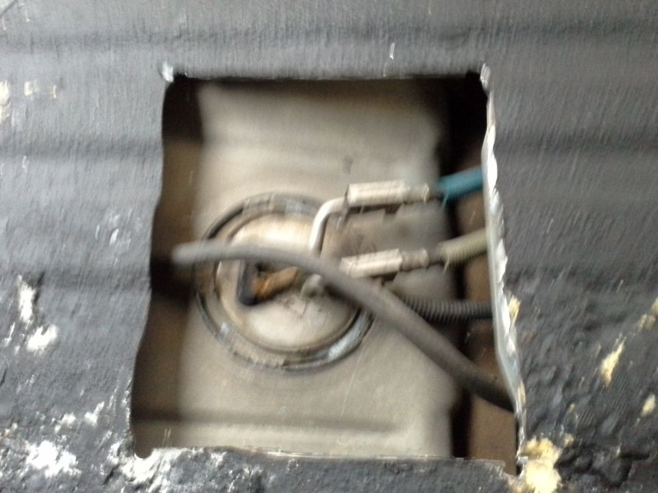 View through a cut-out in the vehicle floor to the fuel tank and fuel lines.